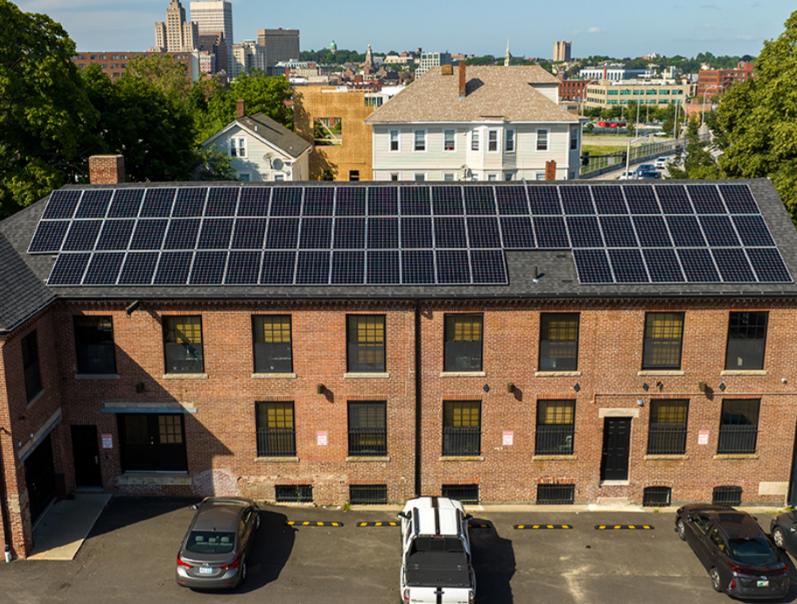 Brick mill building with rooftop solar panels, the photograph beside SAGE's note on the Friendship Street headquarters